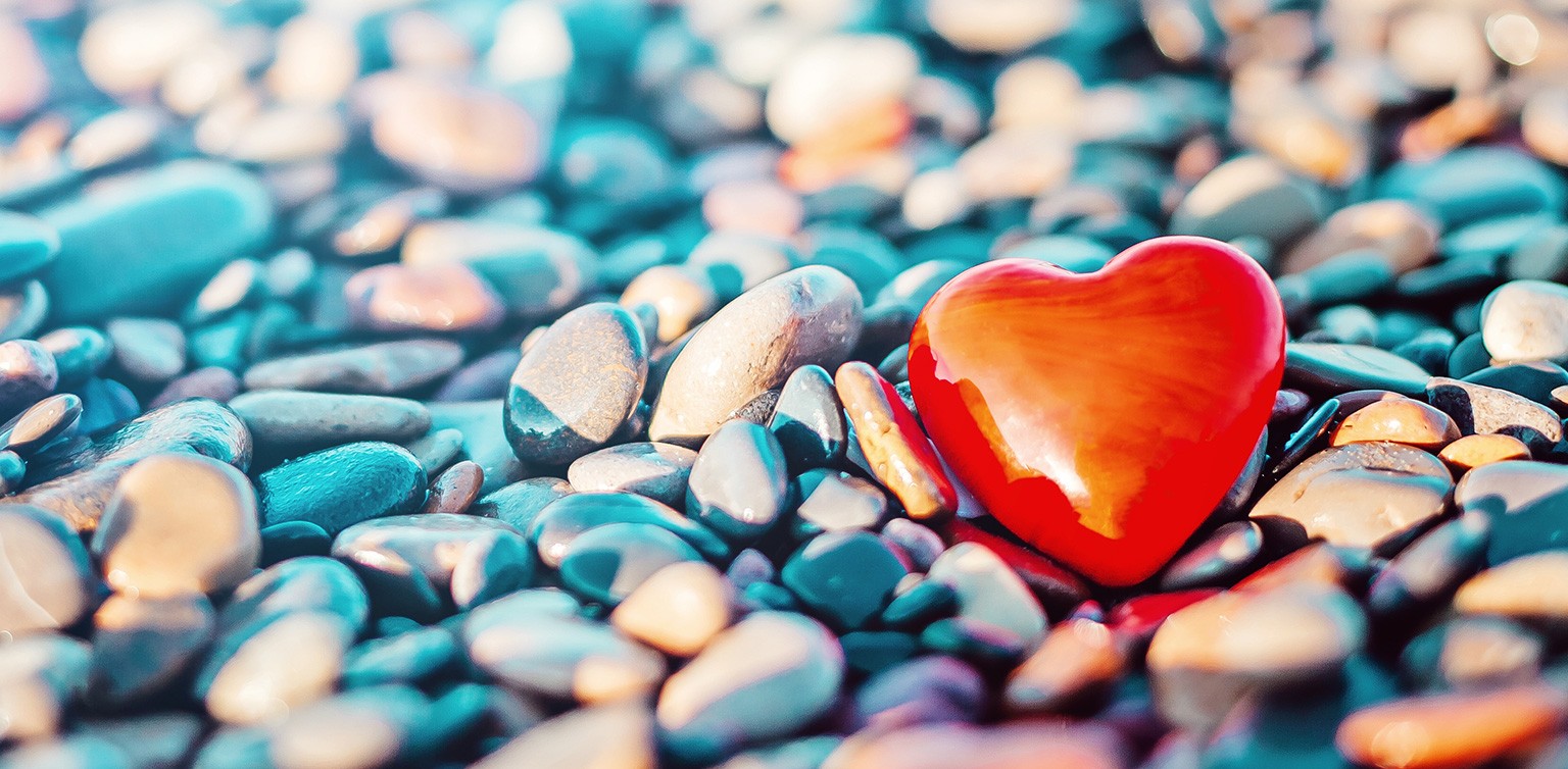 A photo of a red glass heart on a blue and grey pebbled beach 