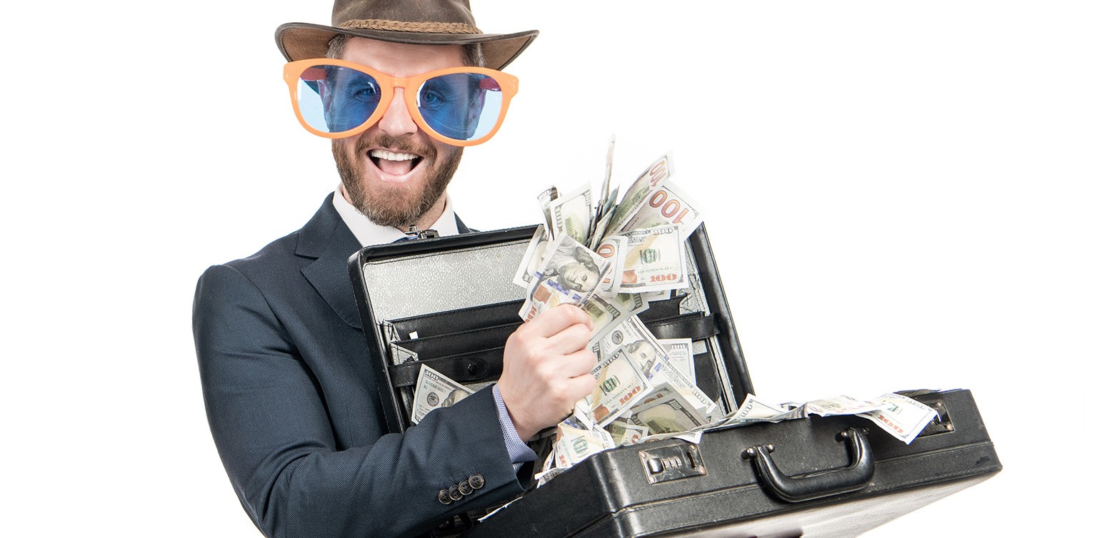 A photo of a bearded man in a suit wearing outsized sunglasses holding an open briefcase stuffed with bank notes on white