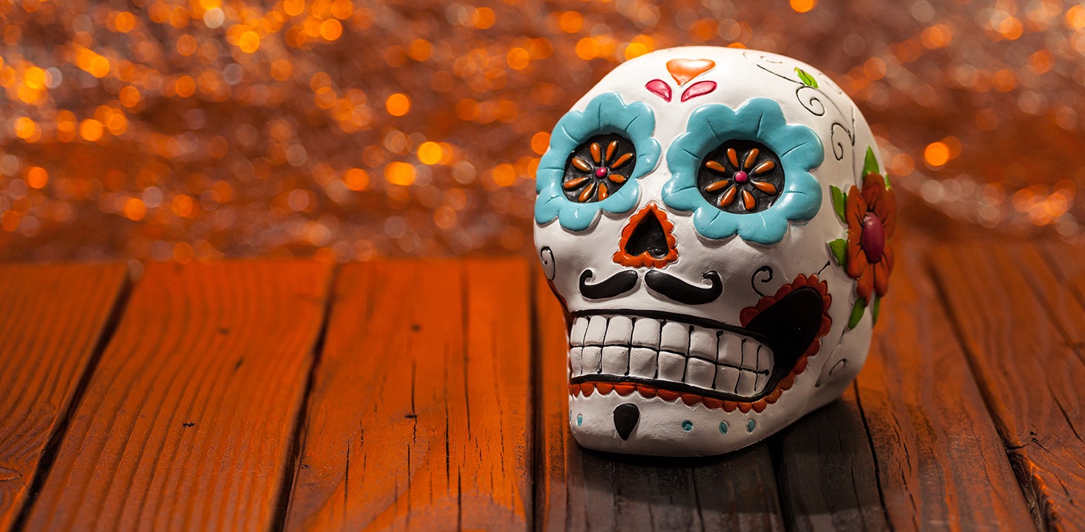 A photo of a colorful Mexican Day of the Dead sugar skull on a wooden table against a golden lit background