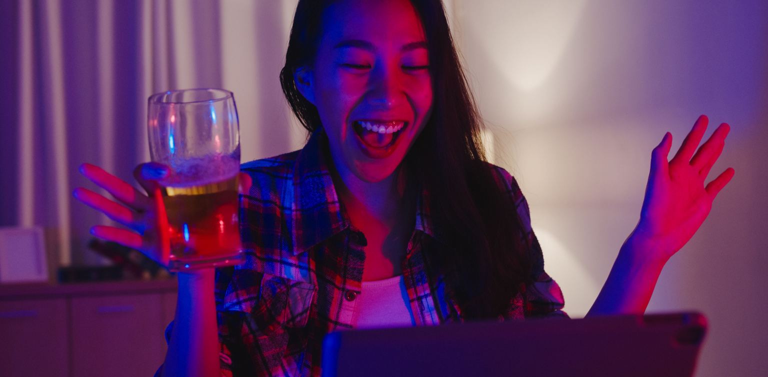 A photo of a lady holding a glass with beer in front of a laptop having a good time